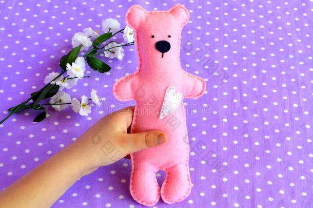 孩子手里拿着一只小毛毡泰迪熊。 粉红色的泰迪熊玩具。 儿童玩具