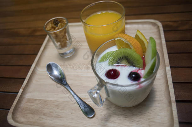 把酸奶布丁放在玻璃杯里，水果装饰，蜂蜜在杯子里，橙汁在木盘上的玻璃杯里