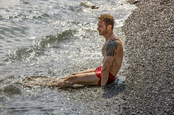 英俊的肌肉男在海滩上躺在砾石上