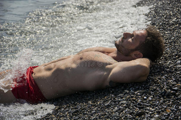 英俊的<strong>肌肉男</strong>在海滩上躺在砾石上