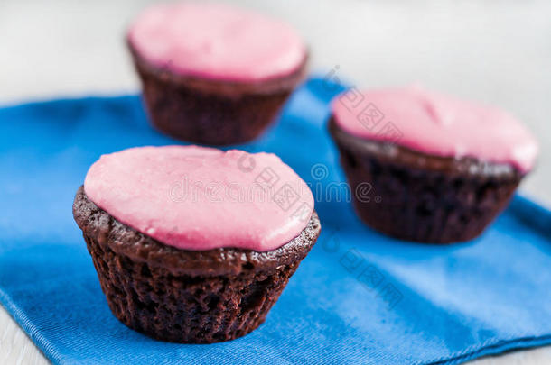 蓝色餐巾纸上有粉红色奶油的巧克力纸杯蛋糕