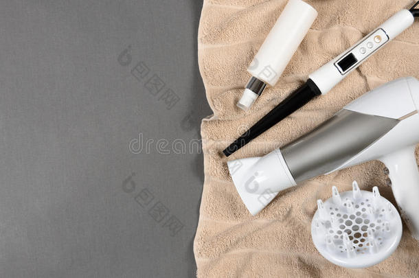 米色毛巾上的发型工具(白色吹风机、发胶、喷雾、锥形卷发棒。 上面的风景