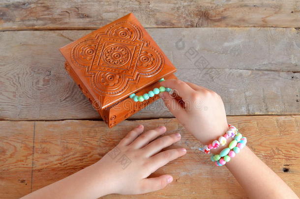 女孩戴着手镯。 孩子们的手把手镯放在木箱里。 旧的木制背景
