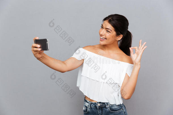 女孩在智能手机上拍自拍照片，并显示良好的手势