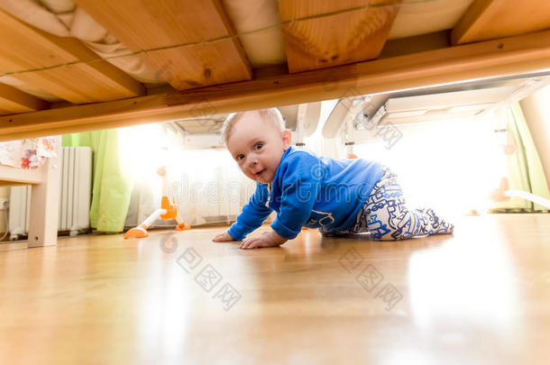 小男孩爬在地板上，看着床<strong>底下</strong>