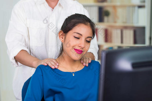 迷人的黑发办公室妇女穿着蓝色毛衣坐在办公桌旁接受肩部按摩，<strong>缓解压力</strong>的概念