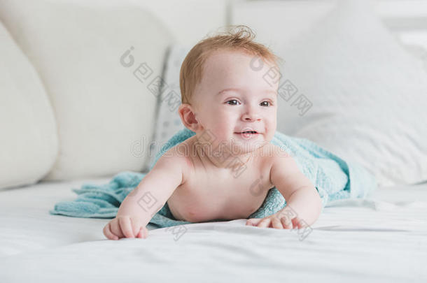 可爱的微笑婴儿在蓝色毛巾淋浴后爬行在床上