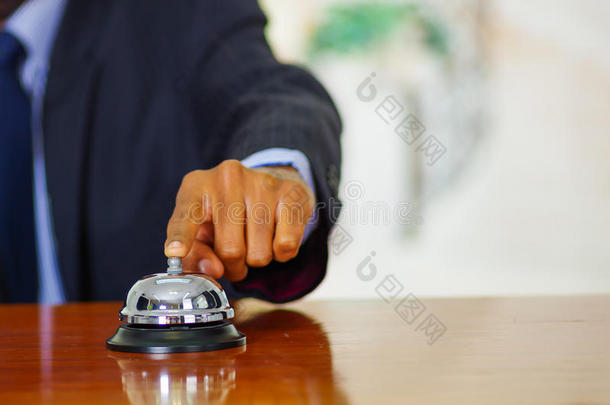 在酒店接待处，穿着蓝色西装的男人的特写手臂按着桌子铃