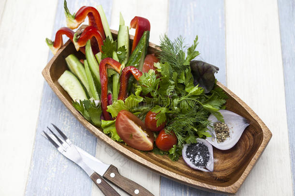 用叉子和刀在木制盘子上的新鲜蔬菜。 红辣椒，番茄，黄瓜，萝卜，欧芹，迪尔健康饮食。