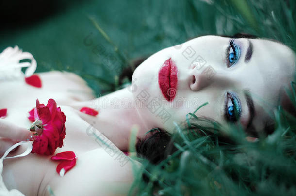 特写深褐色女人的肖像，躺在草地上，嘴唇<strong>红红</strong>的，到处都是玫瑰花瓣。 美丽，时尚的概念。