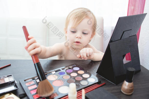 可爱的小女孩带着化妆品和镜子。
