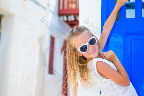 可爱的女孩穿着白色连衣裙在户外，在旧街道上，一个米科诺斯。 典型的希腊传统村庄的街道上的孩子