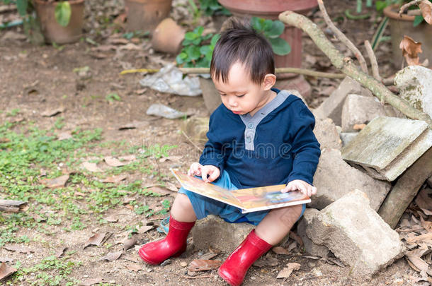 亚洲男孩阅读故事书，男孩穿红色靴子坐