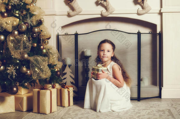 女孩带着礼品盒坐在圣诞树附近，复<strong>古色</strong>调