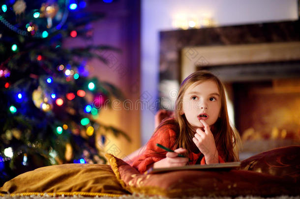 可爱的小女孩在圣诞节的壁炉旁给圣诞老人写了一封信