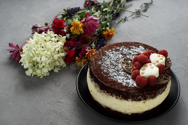 蛋糕上覆盖着巧克力装饰的覆盆子，灰色背景上有一束花。