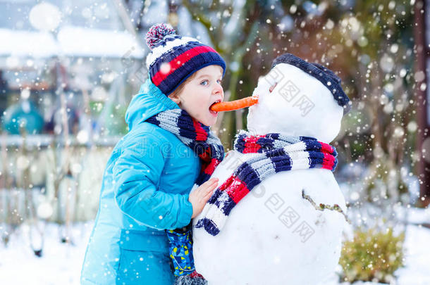 有趣的男孩穿着五颜六色的衣服在户外堆雪人