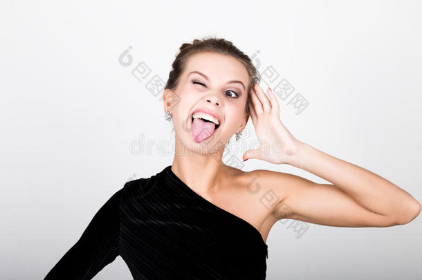 特写时尚照片的年轻女士穿着优雅的黑色连衣裙，嬉戏的女人展示舌头