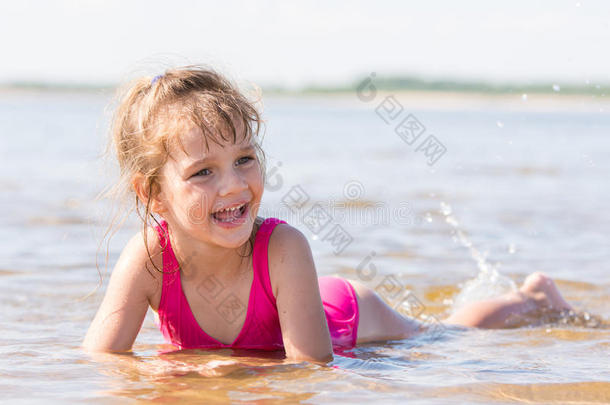 五岁的女孩<strong>躺</strong>在河里的浅滩上，笑<strong>着看着</strong>左边