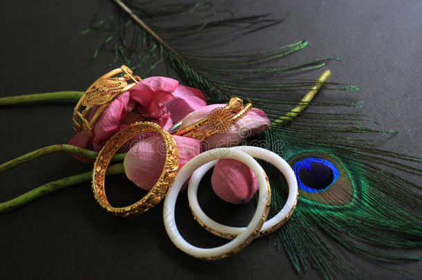 海螺手镯和金色手镯与粉红色莲花和孔雀羽毛在黑色背景。