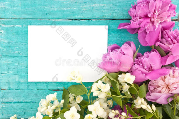 一束粉红色的牡丹花和仿橘红色的花，绿松石色的乡村木纹背景，上面有一张空卡片，用来打招呼。