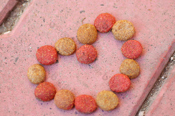 特写新鲜的红色和棕色的脆狗食品躺在石头瓷砖表面，形成心脏