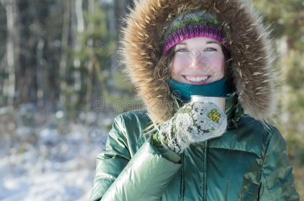冬天森林里开朗的年轻女人在户外拿着不锈钢热水瓶旅游杯