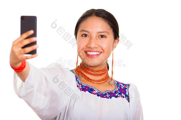 美丽的年轻女人站着，穿着传统的安第斯衬衫和红色项链，拿着手机自拍