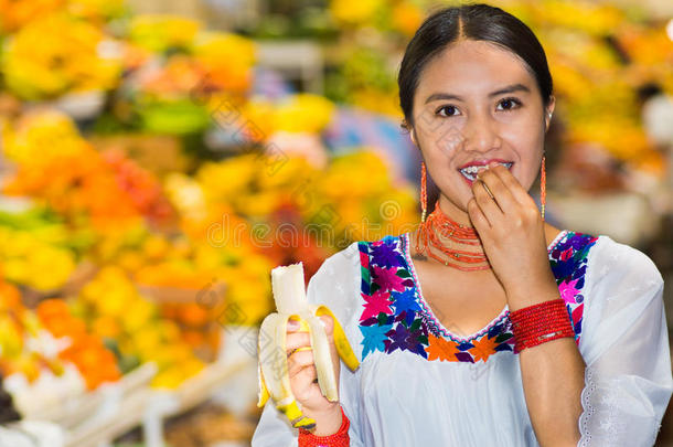 美丽的年轻西班牙女人穿着安第斯传统衬衫，在吃香蕉的水果里摆<strong>姿势拍照</strong>