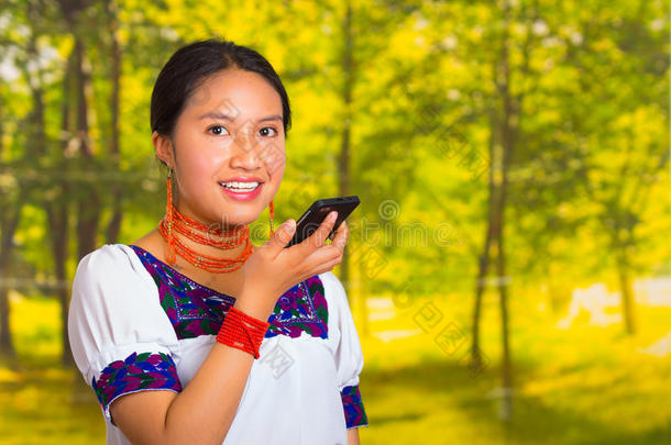 美丽的年轻女人穿着传统的安第斯衬衫，戴着项链，站在镜头前，拿着手机