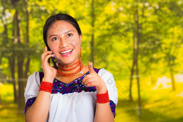 美丽的年轻女人穿着传统的安第斯衬衫，戴着项链，站在镜头前，拿着手机