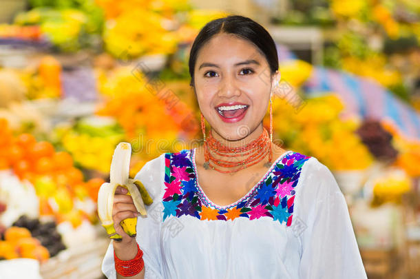 美丽的年轻西班牙女人穿着安第斯传统衬衫，在吃香蕉的水果里摆<strong>姿势拍照</strong>