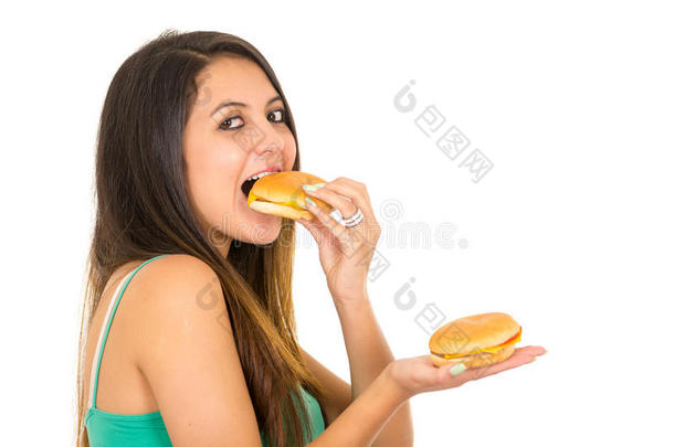 美丽的年轻女人摆着姿势，准备拍照，一边吃汉堡包，一边拿着另一只手，开心地笑着，白色的