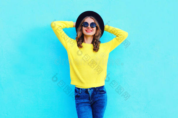时尚快乐，美丽微笑的女人戴着黑色的帽子和黄色的针织毛衣，上面有五颜六色的蓝色