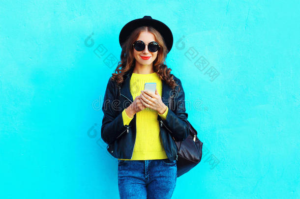 时尚漂亮的女人使用智能手机，穿着黑色的摇滚风格的衣服，穿着五颜六色的蓝色