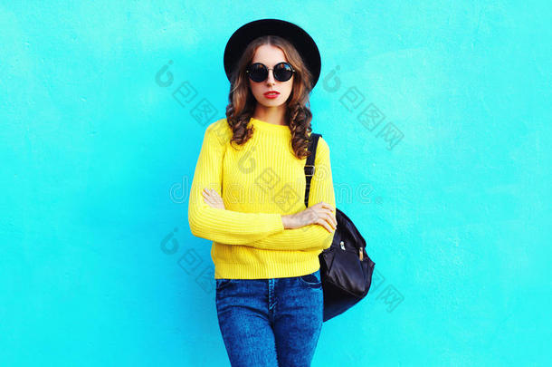 时尚漂亮的女人戴着黑色帽子，黄色针织毛衣背包，上面有五颜六色的蓝色