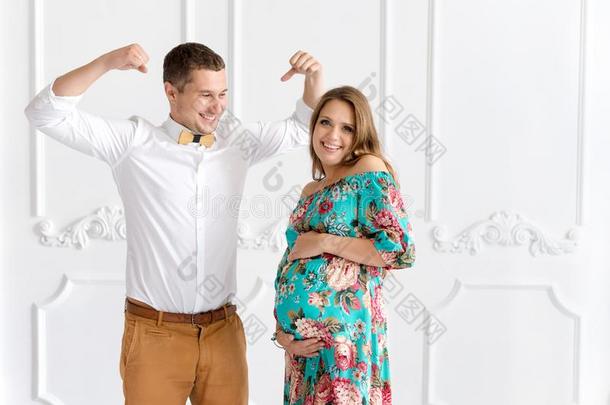 美丽的怀孕夫妇高兴地在一起期待着一个孩子。 穿着白色<strong>简约</strong>内饰的男人和女人。 男人<strong>展</strong>示他的