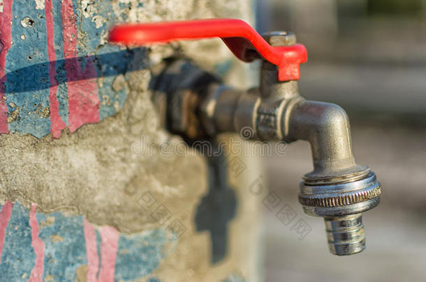 旧蓝色彩绘墙上的水龙头。 红色手柄水龙头室外背景。 节约用水的概念。