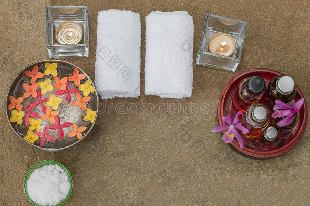 芳香油在木木碗，燃烧的蜡烛，粉红色的黄色橙色花，白色的毛巾在老式的磨碎石背景上