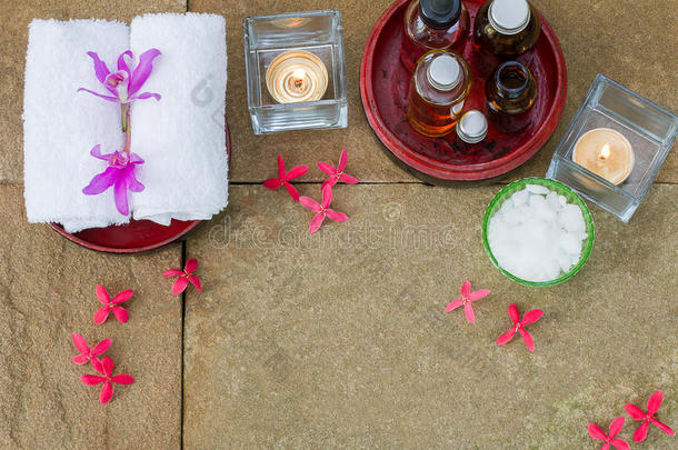 芳香油在磨碎的木碗，燃烧的蜡烛，粉红色的花，白色的毛巾在老式的磨碎石背景上