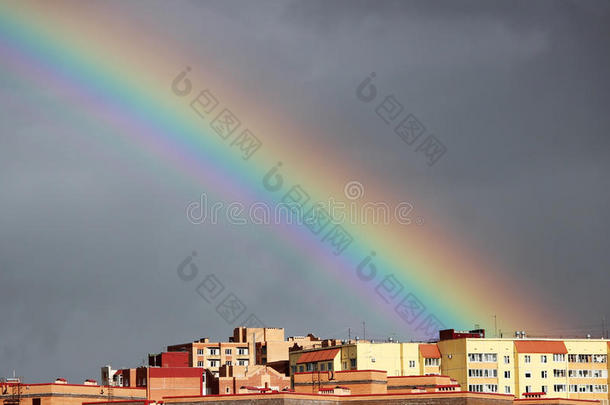 明亮的多色宽阔的彩色彩虹在暴风雨后在灰色的天空上的城镇房屋