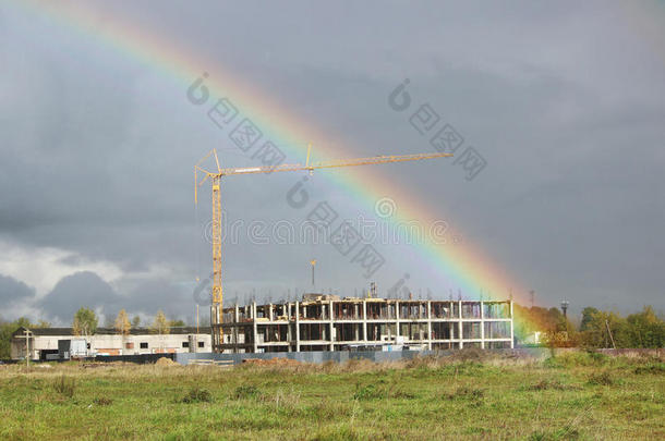 明亮的彩色宽彩虹和一台起重机在建筑工地上的暴风雨后在灰色的天空中。