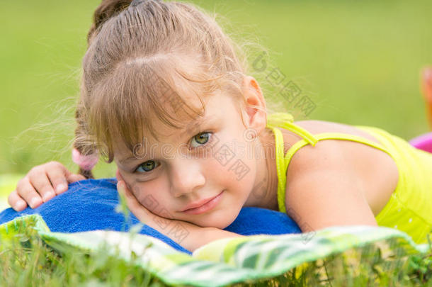 五岁的女孩躺在绿色草地<strong>上</strong>的<strong>一张</strong>床<strong>上</strong>，摸着镜框