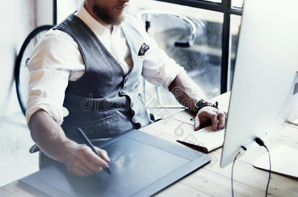特写胡须平面设计师工作图纸数字平板电脑桌面电脑木桌。时尚的年轻人穿着