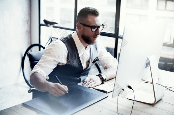 留胡子的创意设计师绘制数字平板<strong>电脑桌面</strong>电脑木桌。时尚的年轻人戴眼镜