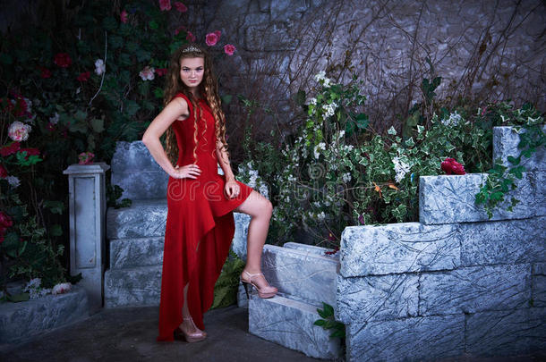 <strong>童话故事</strong>。 穿着红色连衣裙的美丽公主坐在一个神秘的花园里