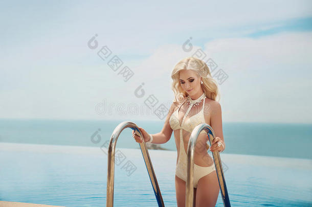 美丽优雅的金发女人，比基尼模特，长金发波浪发型，穿着时尚泳衣，在无限的游泳中摆姿势