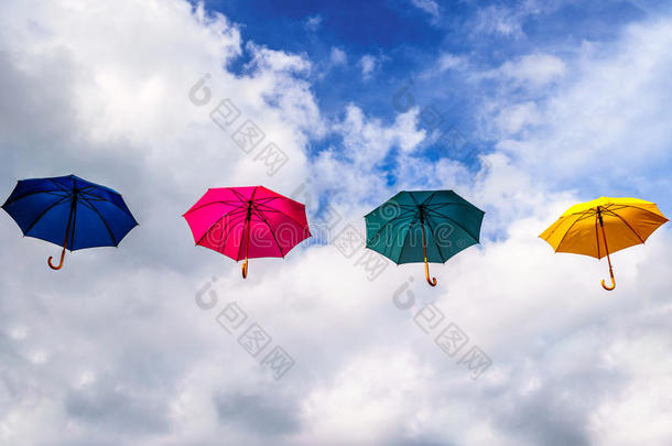 蓝色的伞，红色的伞，绿色的伞和黄色的伞，漂浮在蓝天和云彩的空中