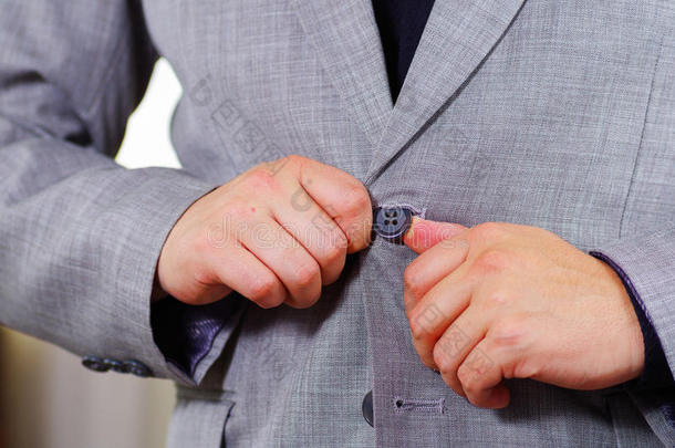 特写男子的胸部区域穿着正式的西装和领带，调整夹克纽扣使用手，男子着装概念