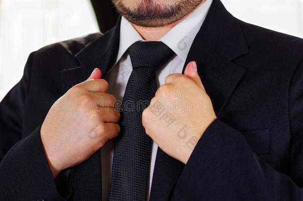 特写男子的胸部区域穿着正式的西装和领带，调整夹克衣领使用手，男子穿衣服的概念